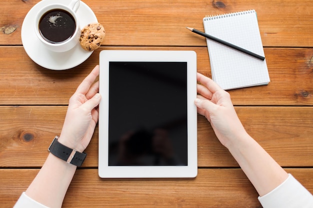 El concepto de negocios, educación, tecnología y personas: cierre de una mujer con una pantalla de computadora de tablet pc en blanco, un cuaderno y un café en una mesa de madera