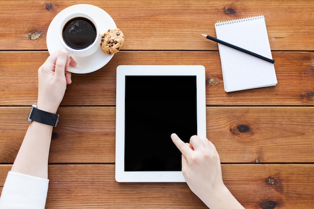 El concepto de negocios, educación, tecnología y personas: cierre de una mujer con una pantalla de computadora de tablet pc en blanco, un cuaderno y un café en una mesa de madera