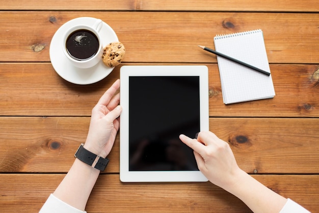 El concepto de negocios, educación, tecnología y personas: cierre de una mujer con una pantalla de computadora de tablet pc en blanco, un cuaderno y un café en una mesa de madera