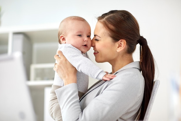 concepto de negocios, maternidad, multitarea, familia y personas: feliz mujer de negocios sonriente con un bebé en la oficina