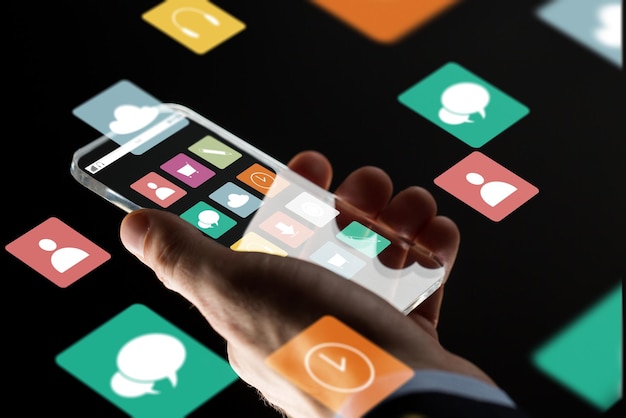 Concepto de negocios, multimedia, personas y tecnología moderna: primer plano de la mano de un hombre de negocios con un teléfono inteligente transparente con iconos de menú en la pantalla sobre fondo negro