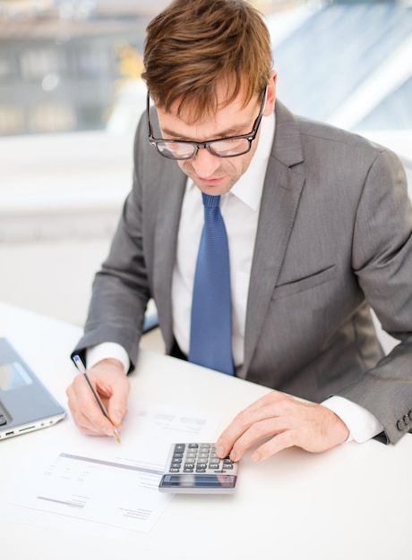 concepto de negocios, oficina, escuela y educación - hombre de negocios con computadora portátil, papeles y calculadora