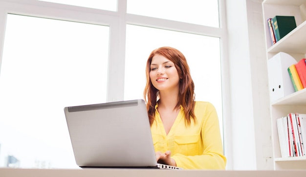 concepto de negocios, oficina, escuela y educación - mujer de negocios sonriente con computadora portátil en la oficina