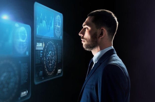 Concepto de negocios, personas, big data y tecnología: hombre de negocios con traje mirando la proyección de pantallas virtuales sobre fondo negro