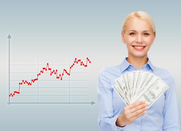 concepto de negocios, personas y dinero - mujer de negocios sonriente con dinero en efectivo en dólares sobre fondo gris y gráfico de forex subiendo