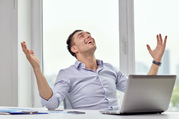 concepto de negocios, personas, éxito y alegría - hombre de negocios feliz con laptop en la oficina