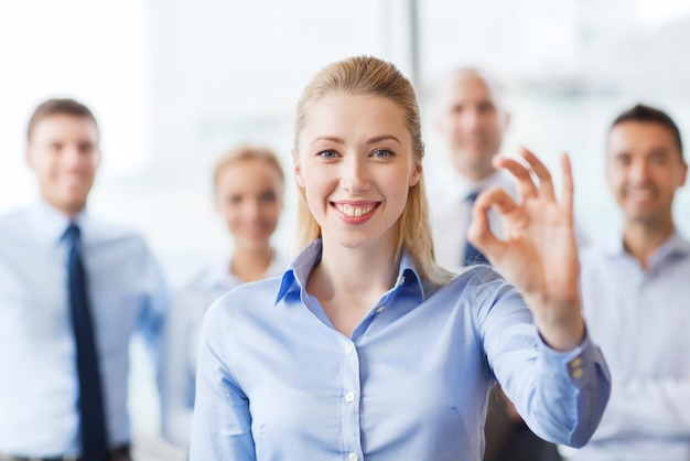 concepto de negocios, personas, gestos y trabajo en equipo - mujer de negocios sonriente que muestra el signo correcto con un grupo de empresarios en el cargo