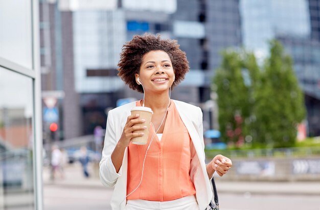 concepto de negocios y personas - joven empresaria afroamericana sonriente con taza de café en la ciudad