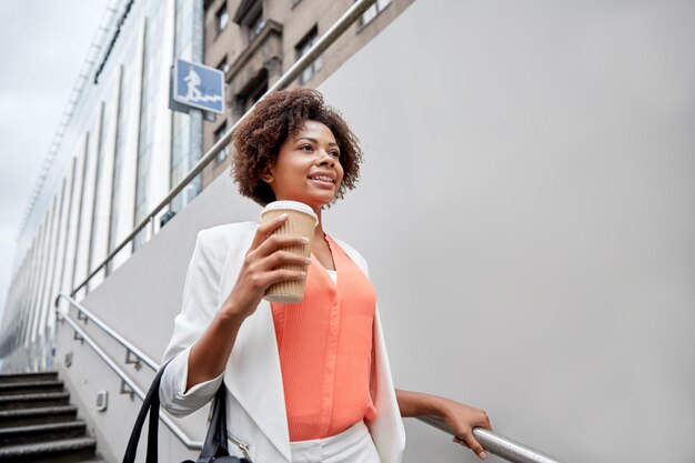 concepto de negocios y personas - joven mujer de negocios afroamericana sonriente con una taza de café bajando las escaleras hacia el paso subterráneo de la ciudad