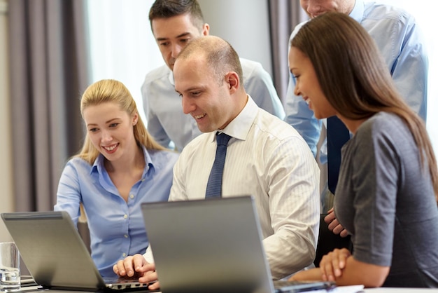 concepto de negocios, personas y tecnología - equipo de negocios sonriente con computadoras portátiles reunidas en la oficina