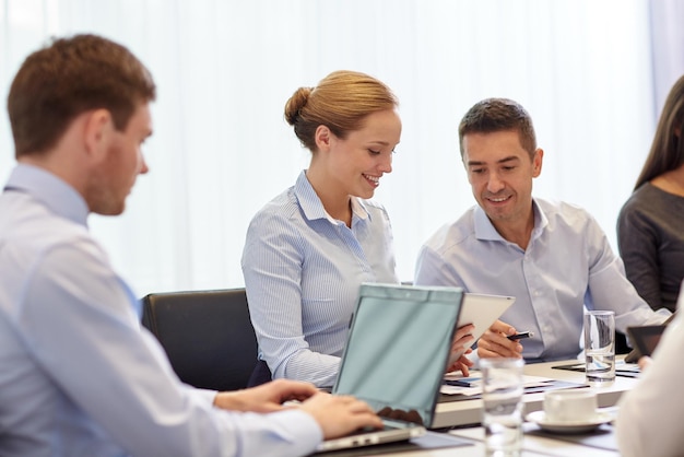 concepto de negocios, personas y tecnología - equipo de negocios sonriente con reunión de computadora portátil y tablet pc en la oficina