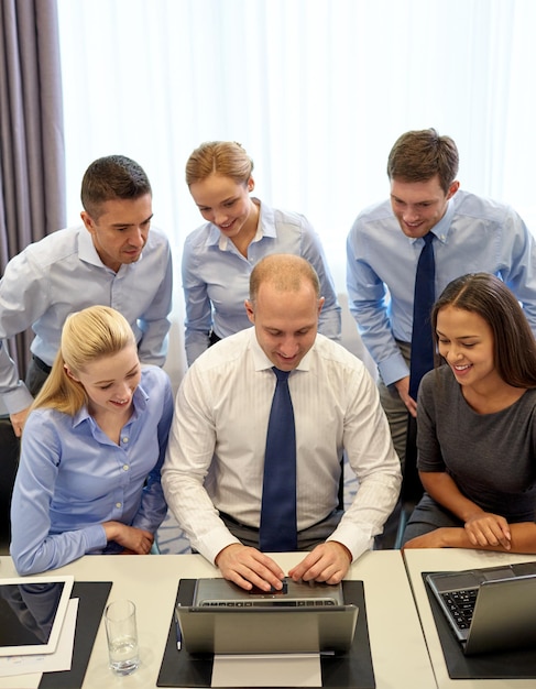 concepto de negocios, personas, tecnología y trabajo en equipo - equipo de negocios sonriente con computadora portátil trabajando en la oficina