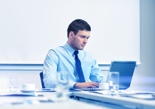 concepto de negocios, personas y trabajo - hombre de negocios con computadora portátil sentado en la oficina frente a la pizarra