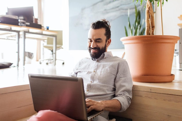 concepto de negocios, puesta en marcha y personas: hombre de negocios feliz o trabajador de oficina masculino creativo con redes de computadoras portátiles