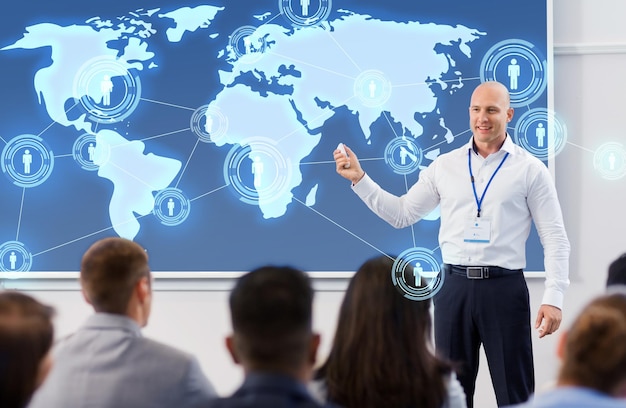 concepto de negocios, red global y personas - empresario o conferenciante sonriente con un mapa del mundo en la pantalla de proyección y un grupo de estudiantes en una presentación de conferencia o conferencia