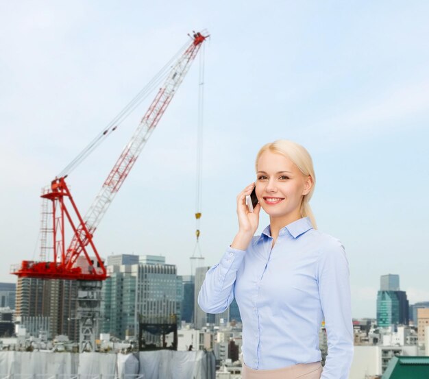 concepto de negocios, tecnología, construcción y personas - joven empresaria sonriente con smartphone sobre fondo de construcción de la ciudad