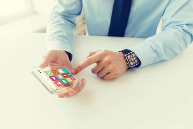 concepto de negocios, tecnología y personas: cierre de la mano masculina que sostiene y muestra un teléfono inteligente transparente y mira en la oficina con iconos de menú en la pantalla