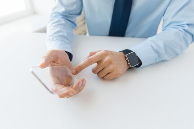 concepto de negocios, tecnología y personas: cierre de la mano masculina sosteniendo y mostrando un teléfono inteligente transparente y un reloj en la oficina