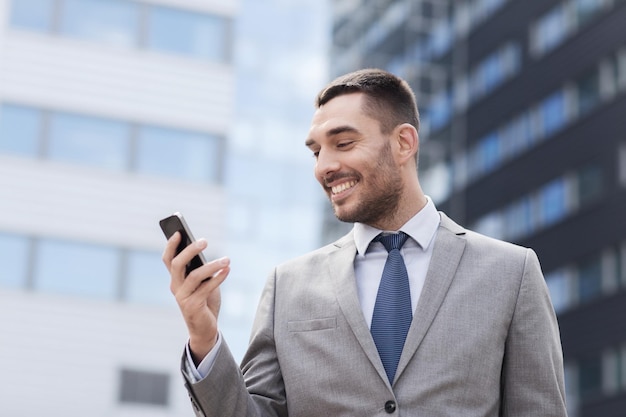 concepto de negocios, tecnología y personas - hombre de negocios sonriente con teléfono inteligente sobre el edificio de oficinas