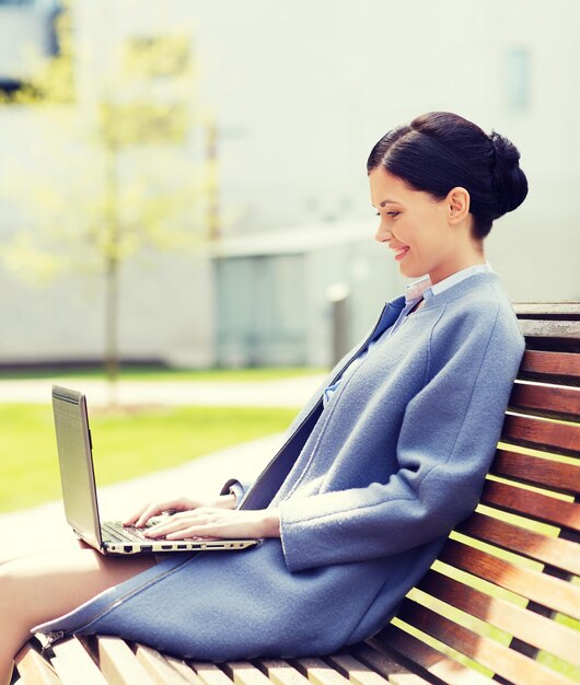 concepto de negocios, tecnología y personas - joven mujer sonriente con computadora portátil sentada en un banco en la ciudad