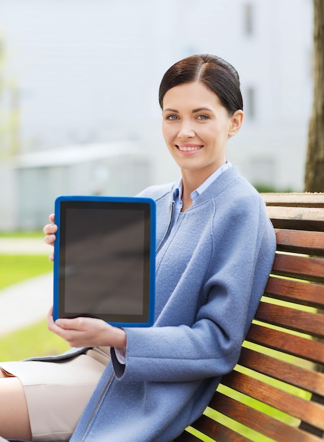 El concepto de negocios, tecnología y personas: una joven sonriente con una computadora de tableta sentada en un banco en la ciudad