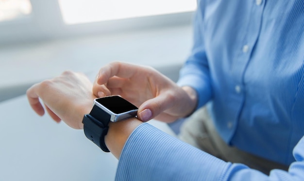 Foto concepto de negocios, tecnología, tiempo y personas - cierre de manos de mujer configurando un reloj inteligente en la oficina