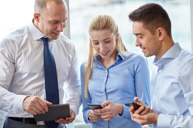concepto de negocios, trabajo en equipo, personas y tecnología: equipo de negocios con tableta y reunión de teléfonos inteligentes en la oficina