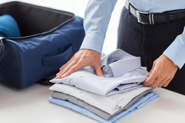 concepto de negocios, viajes, equipaje y personas - hombre de negocios feliz empacando ropa en una bolsa de viaje