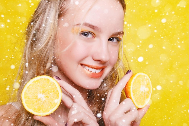 Concepto de nieve, invierno, navidad, emociones, salud, personas, comida y belleza - Beauty Model Girl toma Juicy Oranges. Hermosa chica adolescente alegre con pecas. maquillaje amarillo. sobre fondo de nieve