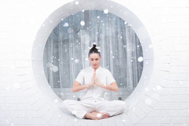 Concepto de nieve, invierno, navidad, fitness, deporte, entrenamiento y estilo de vida - mujer joven haciendo ejercicio de yoga. Retrato joven hermosa en ropa deportiva blanca haciendo práctica de yoga sobre fondo de nieve