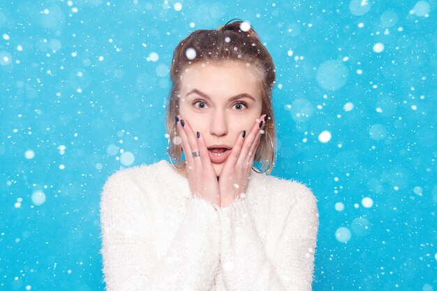 Concepto de nieve, invierno, Navidad, personas, belleza y estilo de vida - Mujer hermosa feliz sorprendida mirando con entusiasmo. sobre fondo de nieve