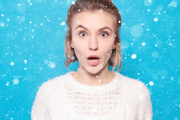 Concepto de nieve, invierno, Navidad, personas, belleza y estilo de vida - Mujer hermosa feliz sorprendida mirando con entusiasmo. sobre fondo de nieve