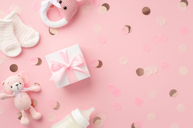 Concepto de niña bebé Vista superior foto de caja de regalo calcetines diminutos tejido conejito sonajero juguete osito de peluche botella de leche de juguete y confeti brillante sobre fondo rosa pastel aislado