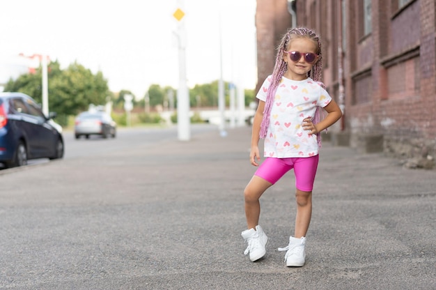 Concepto de niño de moda niña elegante con ropa brillante y gafas de sol contra la pared colorida