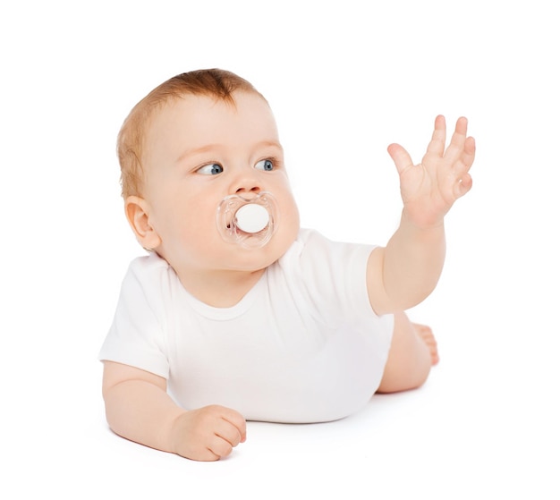 concepto de niño y niño pequeño - bebé sonriente tirado en el suelo con un maniquí en la boca
