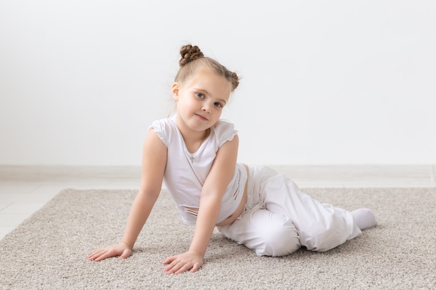 Concepto de niños y niños - niña pequeña vestida con camisa blanca sentada en el suelo con cara pensativa.