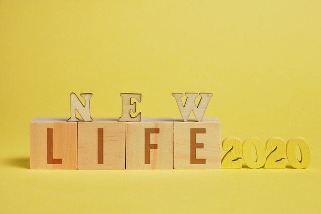 Foto el concepto de una nueva vida. números de madera 2020 junto a cubos con letras sobre un fondo amarillo.