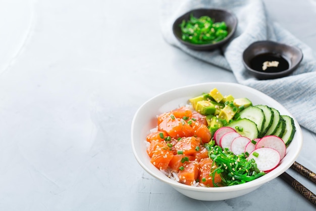 Concepto de nutrición de almuerzo de comida rápida y saludable Tazón de poke de salmón hawaiano orgánico fresco con pepino de aguacate de algas de arroz en una mesa de cocina moderna Fondo de espacio de copia