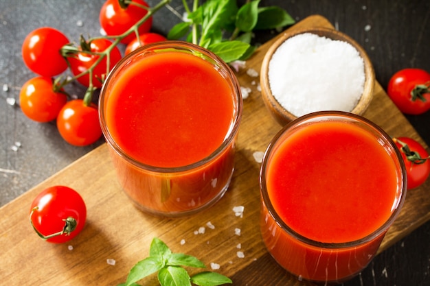 Concepto de nutrición de la dieta Gafas con jugo de tomate closeup y tomates frescos sobre una mesa de piedra oscura