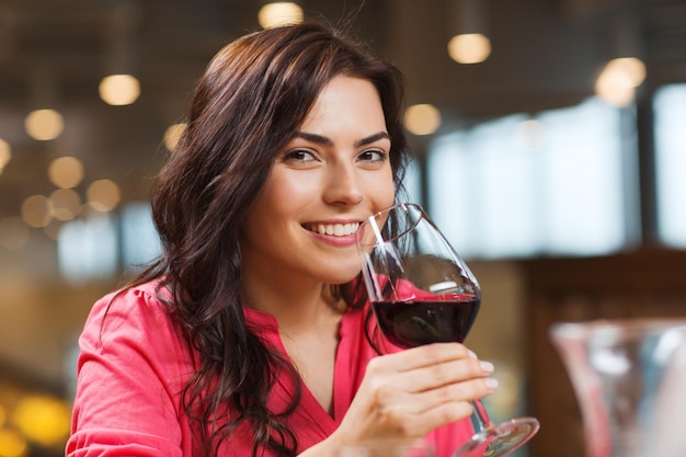 concepto de ocio, bebidas, degustación, gente y vacaciones - mujer sonriente bebiendo vino tinto en el restaurante