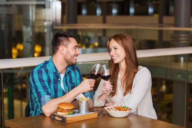 concepto de ocio, celebración, comida y bebida, gente y vacaciones - pareja sonriente cenando y bebiendo vino tinto en una cita en el restaurante