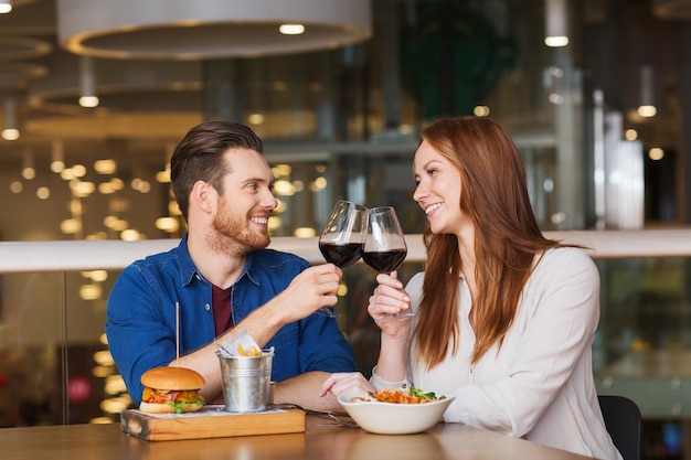 concepto de ocio, celebración, comida y bebida, gente y vacaciones - pareja sonriente cenando y bebiendo vino tinto en una cita en el restaurante