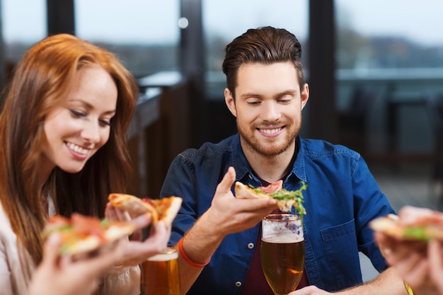 concepto de ocio, comida y bebida, gente y vacaciones - amigos sonrientes comiendo pizza y bebiendo cerveza en un restaurante o pub