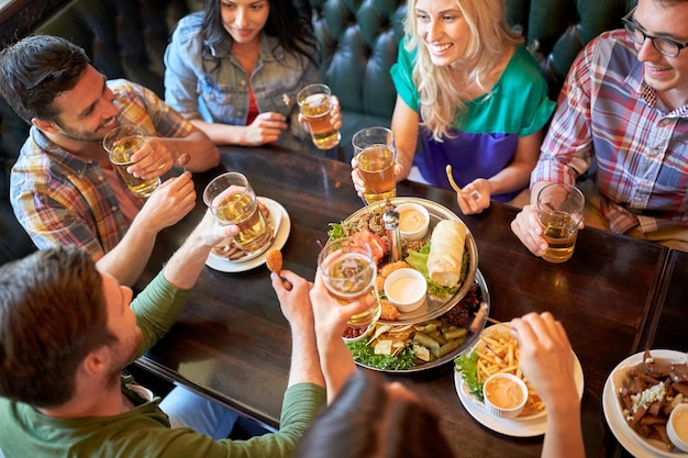 Foto concepto de ocio, comida, bebidas, gente y vacaciones - amigos felices comiendo bocadillos y bebiendo cerveza en el bar o pub