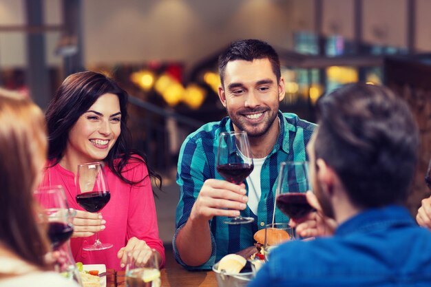 concepto de ocio, comida, comida y bebida, gente y vacaciones - amigos sonrientes cenando y bebiendo vino tinto en el restaurante