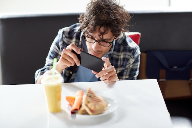 concepto de ocio, comida, comida y personas - hombre con smartphone fotografiando su almuerzo en el café