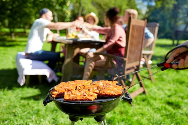 concepto de ocio, comida, gente y vacaciones - hombre cocinando carne en la parrilla para sus amigos en la fiesta de verano al aire libre