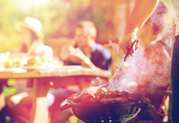 Foto concepto de ocio, comida, gente y vacaciones: hombre cocinando carne en una parrilla para sus amigos en una fiesta de verano al aire libre