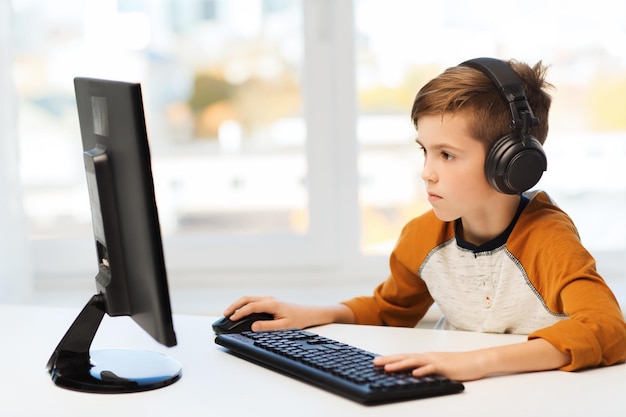 concepto de ocio, educación, niños, tecnología y personas - niño con computadora y auriculares escribiendo en el teclado o jugando videojuegos en casa