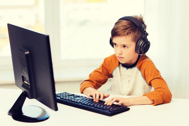concepto de ocio, educación, niños, tecnología y personas - niño con computadora y auriculares escribiendo en el teclado o jugando videojuegos en casa